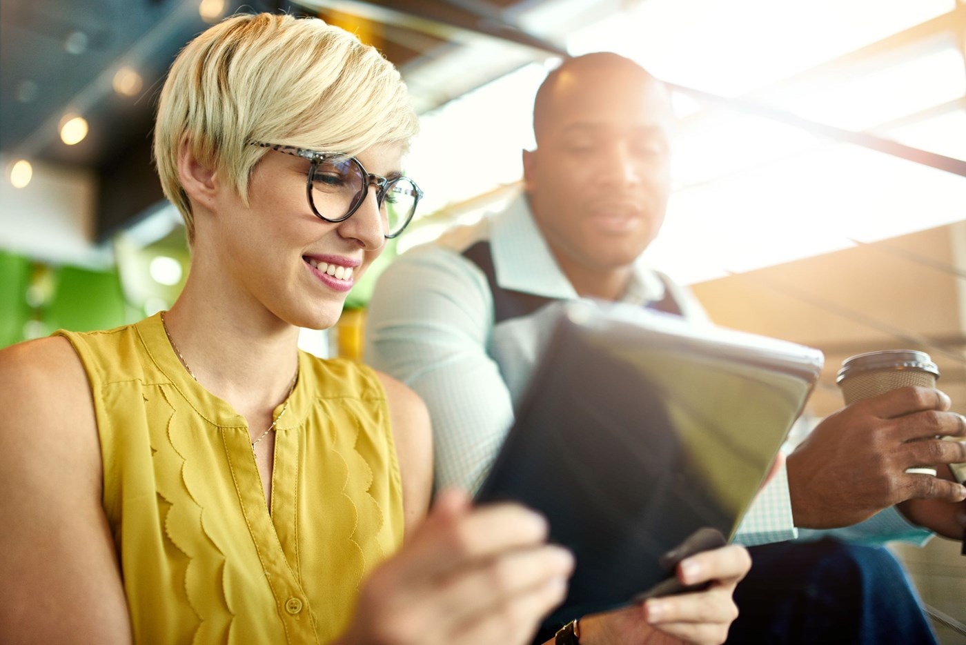 Female in yellow top wearing eyeglasses on tablet beside male
