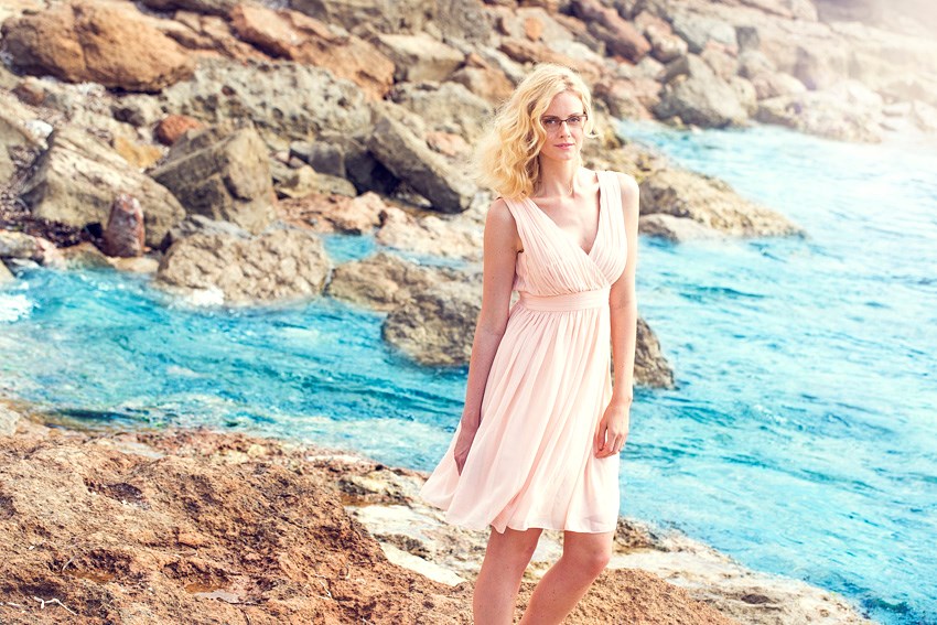 Woman in pink dress wearing eyeglasses on beach beside sea