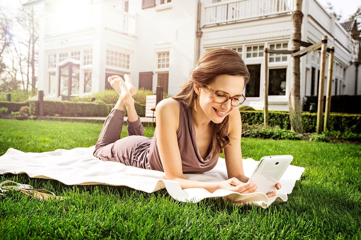Female wearing eyeglasses lying on rug on grass on tablet