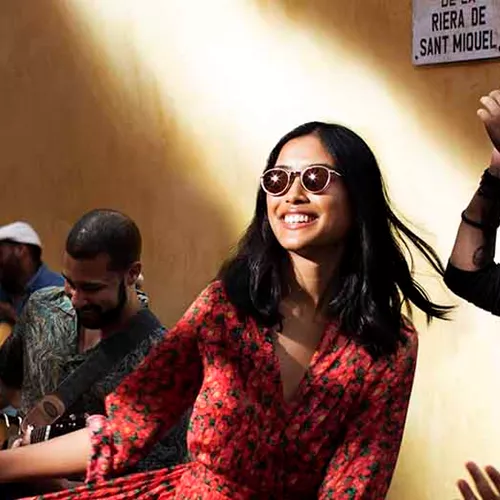 Female wearing sunglasses dancing in street surrounded by people